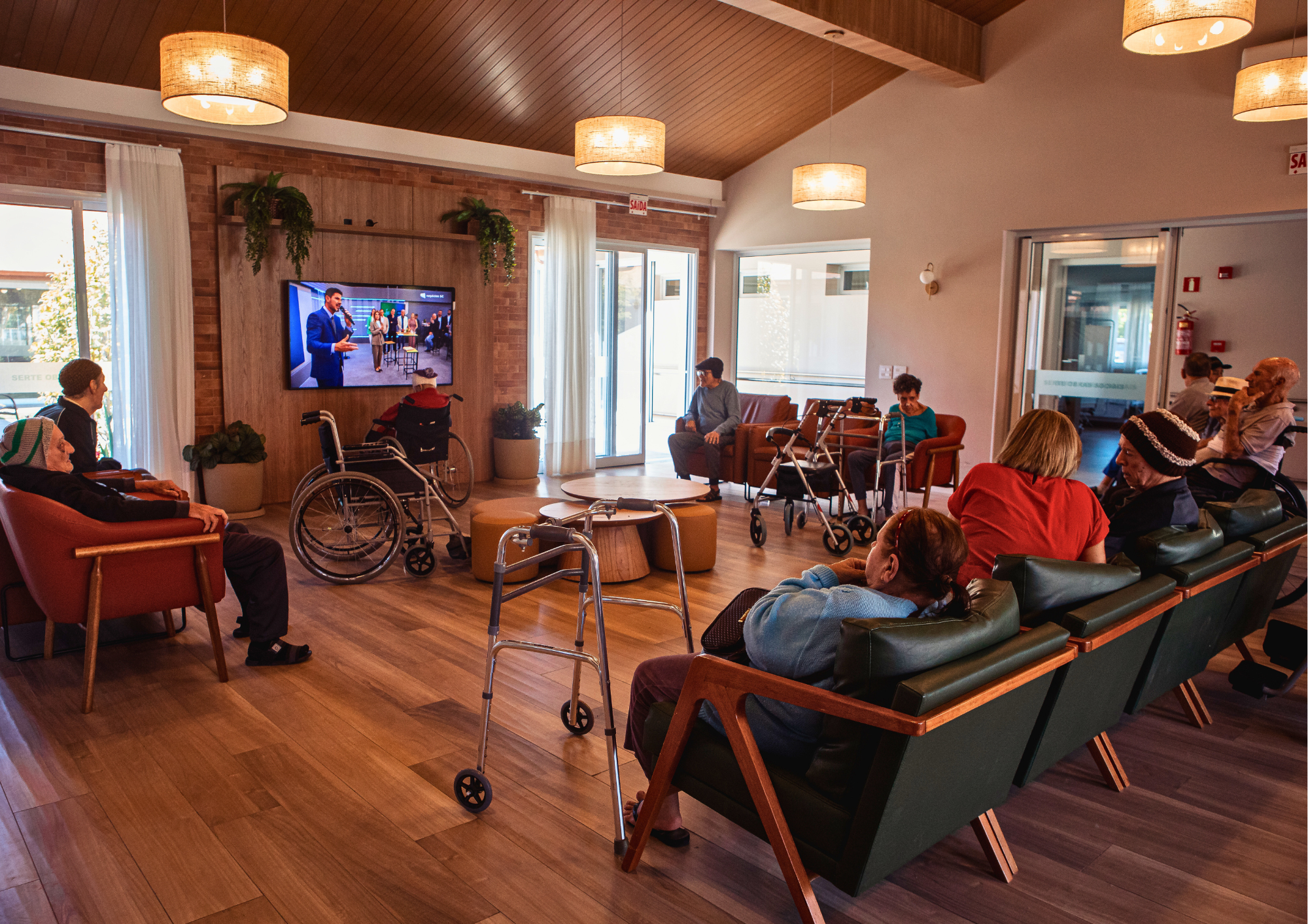 idosos assistindo TV, convivência entre idosos, momento de lazer, sala de estar do lar de idosos, instituição de longa permanência, bem-estar na terceira idade, atividades recreativas, grupo de idosos, vida em comunidade, conforto e acolhimento, descanso e convivência, qualidade de vida do idoso, rotina no lar de idosos, socialização na terceira idade, lazer e companhia